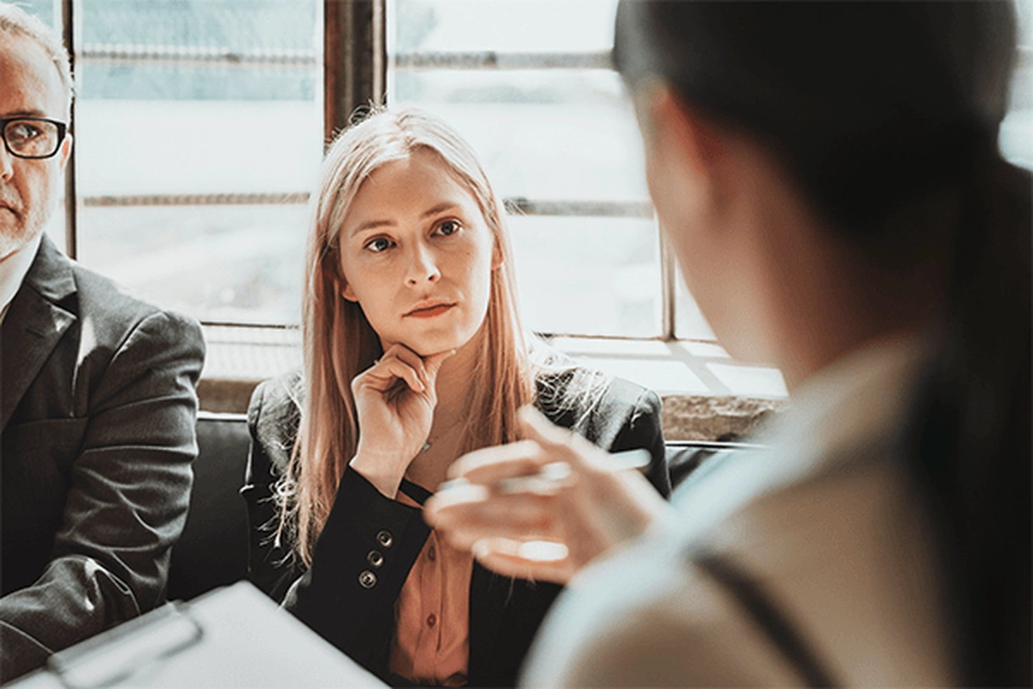 Mediation Köln Süd – Dieses Bild zeigt eine professionelle Geschäftssituation mit einer konzentrierten Frau im Gespräch mit Kollegen, vermutlich in einem Meeting, Vorstellungsgespräch oder einer Beratungssitzung.